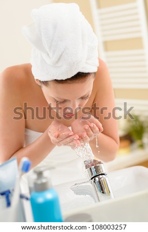 Woman washing face with water above bathroom sink