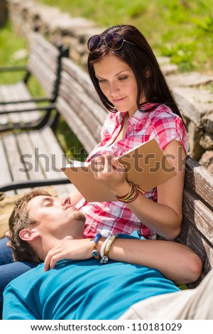 Young happy couple relax on park bench woman read book