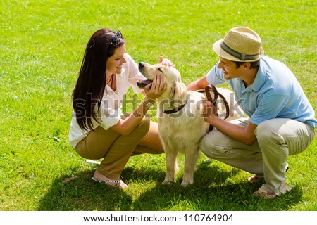 Young happy couple playing with Labrador dog smiling in park