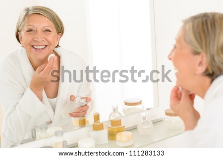 Senior woman smiling cleaning face make-up removal bathroom mirror reflection