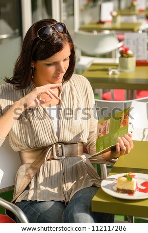 Woman at cafe bar terrace choosing from menu sunny day