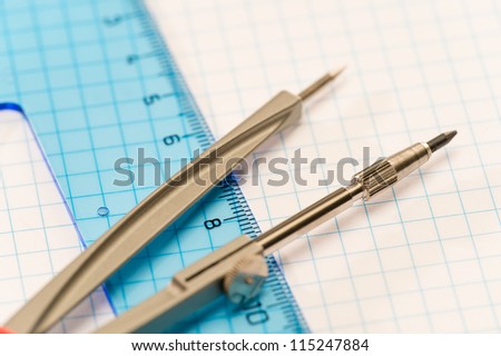 Geometry accessories compasses with blue ruler on square paper