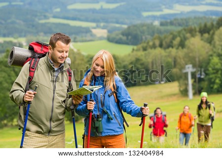 Young hiking couple with friends looking map to find track