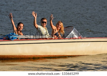 Young people waving from motorboat enjoying summer break