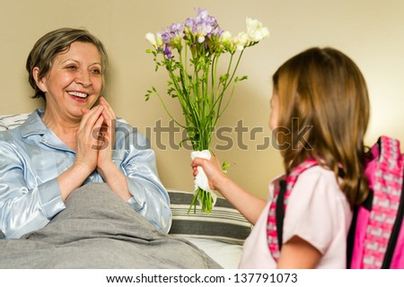 Grandchild giving bouquet of flowers to grandmother lying in bed