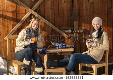 Two young women enjoy tea winter cottage wooden sunny outdoor