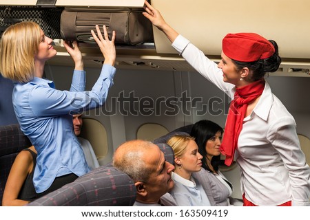 Friendly flight attendant helping passenger to put luggage cabin compartment