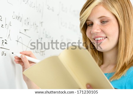 Student girl writing maths on white board looking in book