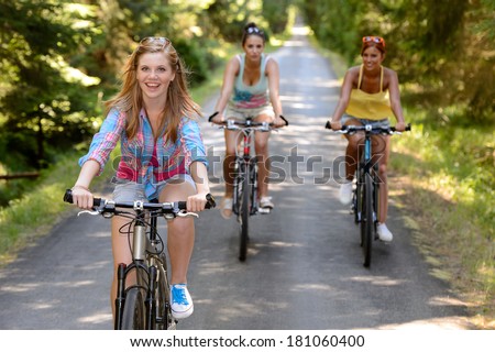 Three female friends riding bikes in park enjoy summer sport