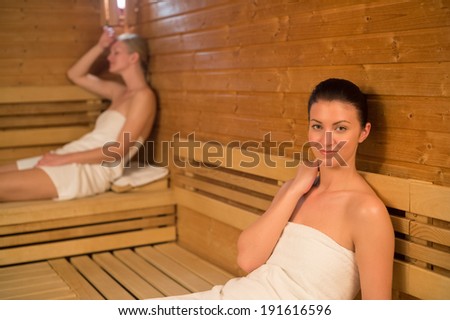 Woman relaxing in sauna with friend in background