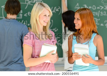 Two college student friends talking front of green chalkboard mathematics