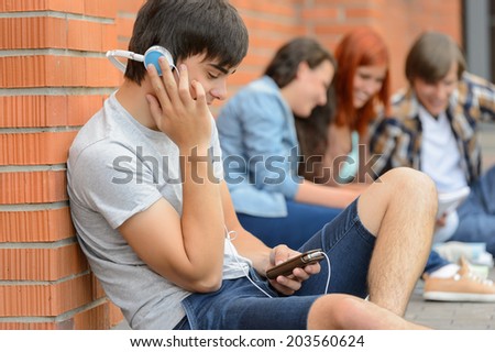 Student boy with headphones college friends sitting outside campus chatting
