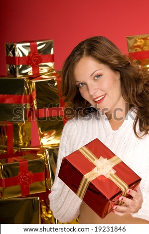 Beautiful brunette offering a Christmas gift in front of pile of gifts