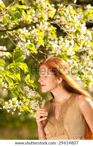 Beautiful red hair woman in brown dress standing under blossom tree enjoying the smell in spring
