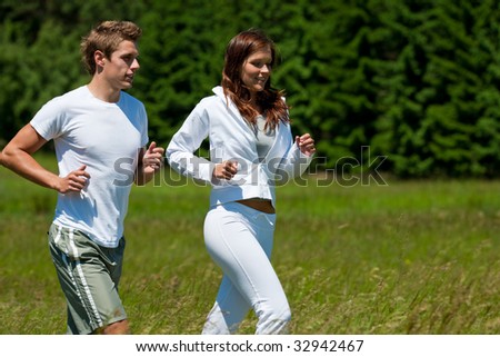 Young man and woman running outdoors on a sunny day, shallow DOF