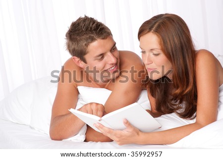 Young man and woman lying down on white sofa, woman reading book