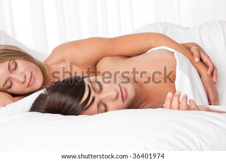Two young women lying down in white bed and sleeping together naked