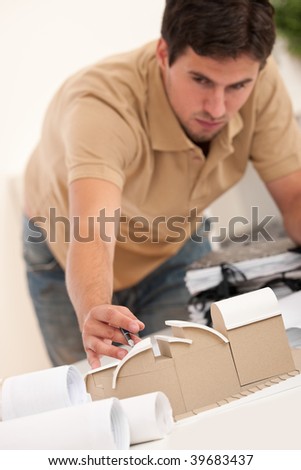 Young male architect working with plans and architectural model at office