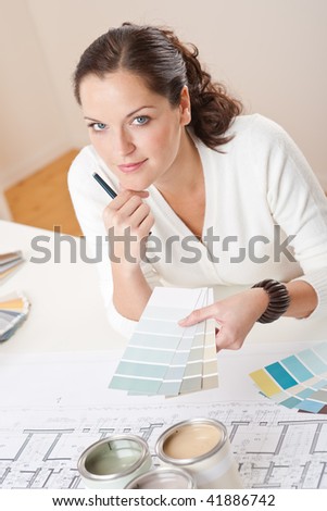 Young female interior designer working at office with color swatch and can of paint