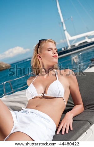 Blond woman sunbathing in white bikini on luxury yacht on the sea