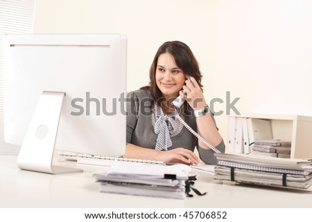 Attractive secretary on phone at office in front of computer screen