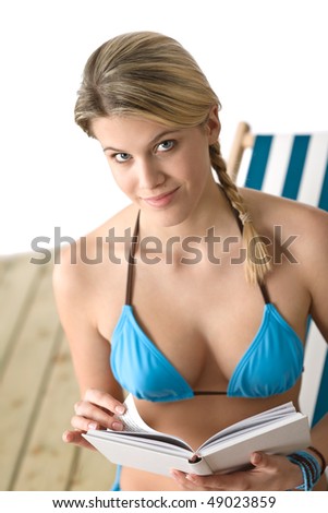 Beach - Happy young woman with book sitting on deck chair in bikini