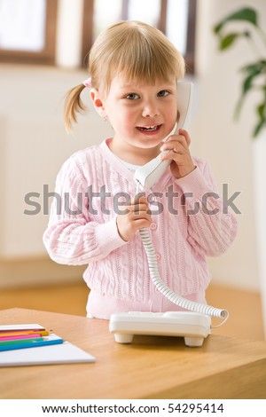 Smiling little girl on phone in lounge holding telephone receiver