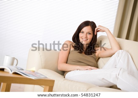 Young woman with magazine and coffee in lounge on sofa