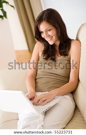 Smiling woman sitting with laptop on sofa in lounge