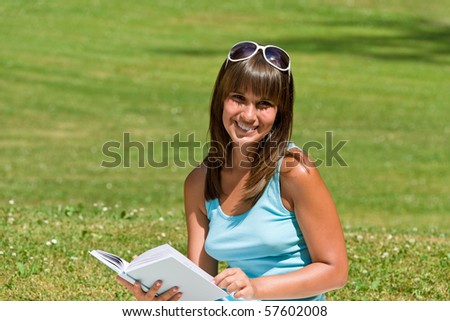 Smiling young woman read book in park on sunny day