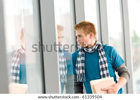 Male teenager holding book standing in modern glass building