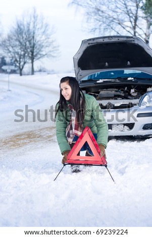 Winter car breakdown - woman placing warning triangle