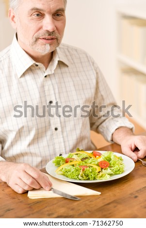 Senior mature man eat vegetable salad at wooden table