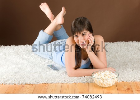 Woman teenager watch television eat popcorn lying on floor