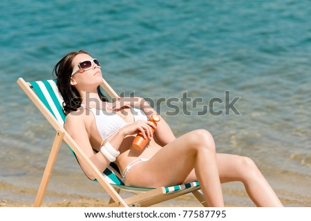 Summer young woman sunbathing in bikini on beach suncream