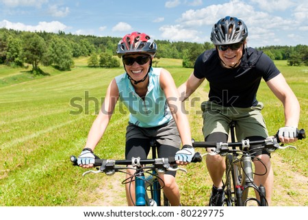 Sport mountain biking - man pushing young girl uphill sunny countryside