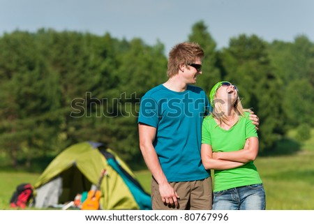 Young camping couple hugging in summer countryside tent in background
