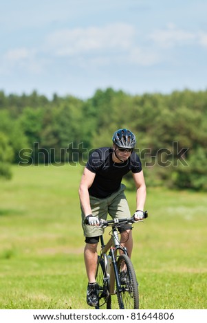 Fit young man cycling uphill mountain bike in summer countryside