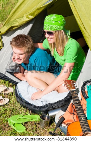 Happy camping couple lying inside tent backpack in sunny countryside