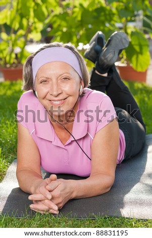 Senior sportive woman on mat listen music outside sunny day