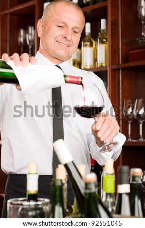 At the bar - waiter pour red wine in glass restaurant