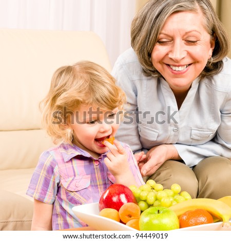 Little girl eat apricot fruit with grandmother relaxing on sofa