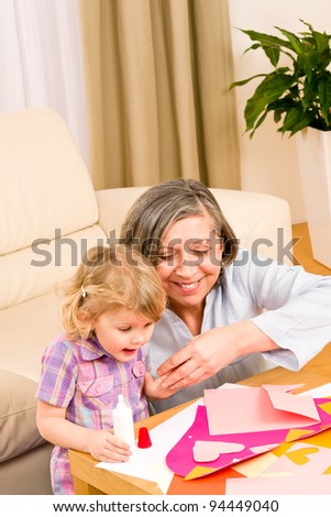 Grandmother with granddaughter playing together glue hearts on paper