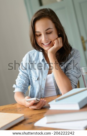 Smiling teenage girl looking at mobile phone studying at home