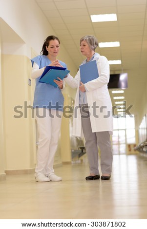 Two female doctors standing watching patient files in hospital corridor