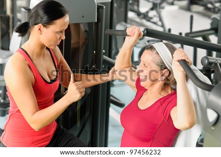 Personal trainer assist senior woman exercising on machine at gym