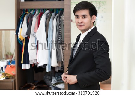 Handsome businessman man wearing a suit in front of wardrobe in the fitting room.