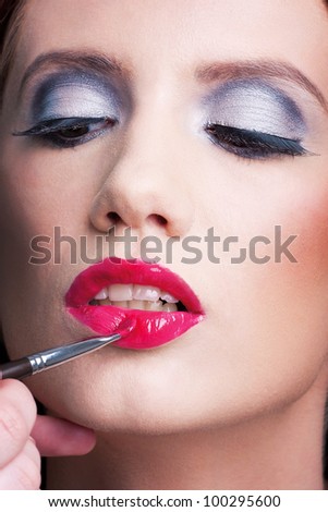 A make-up artist applying a lip stick on a beautiful woman's face