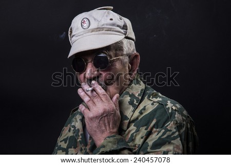 old man in sunglasses and camouflage smokes a cigarette