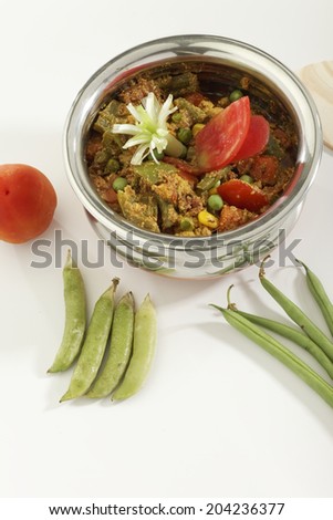 Mix vegetable in steel pot with raw vegetables on white background.